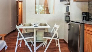 Een kleine keuken met een eettafel, stoelen, een koelkast, een magnetron en een televisie.