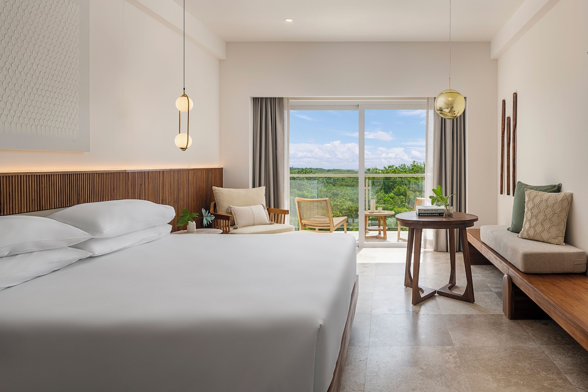 Una habitación de hotel moderna con una cama grande, una zona de estar con una mesa y un balcón con vistas.