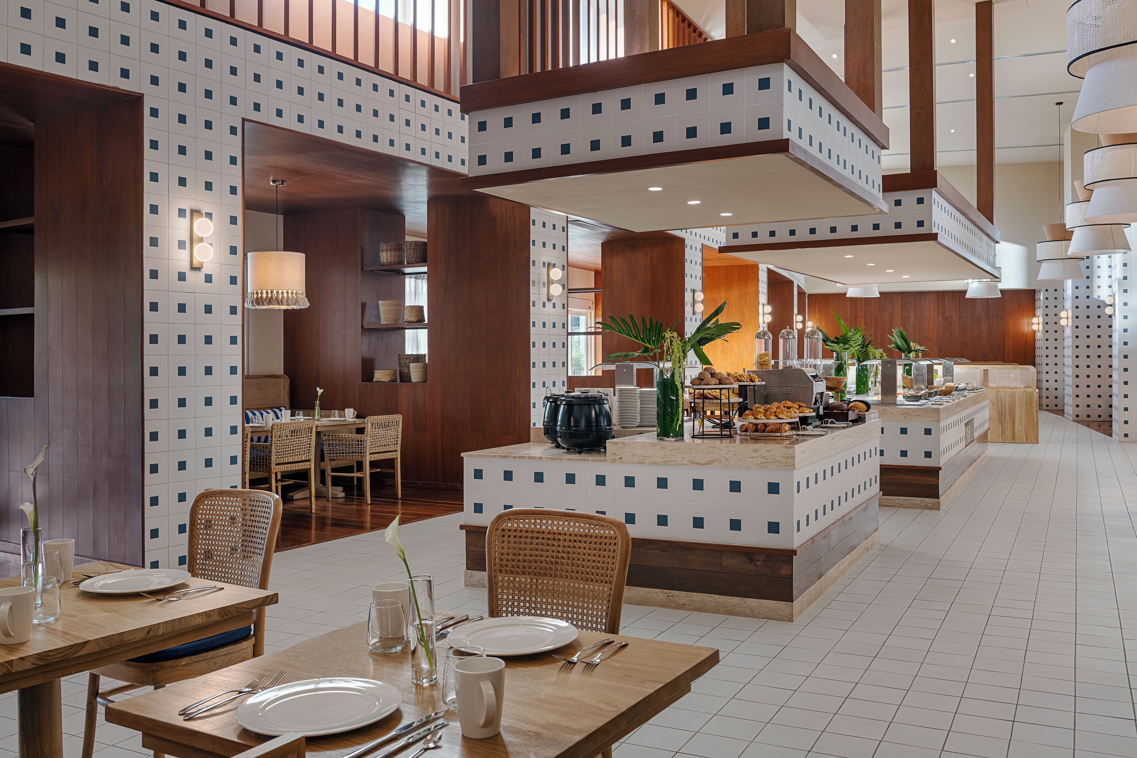 Un amplio vestíbulo de hotel con una isla central, zona de comedor con mesas y sillas, y vistas al área de la cocina.