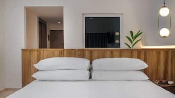 A hotel room with a wooden headboard, a bed with white linens, a bedside table with a book and a bowl, and a wall-mounted mirror with lights.