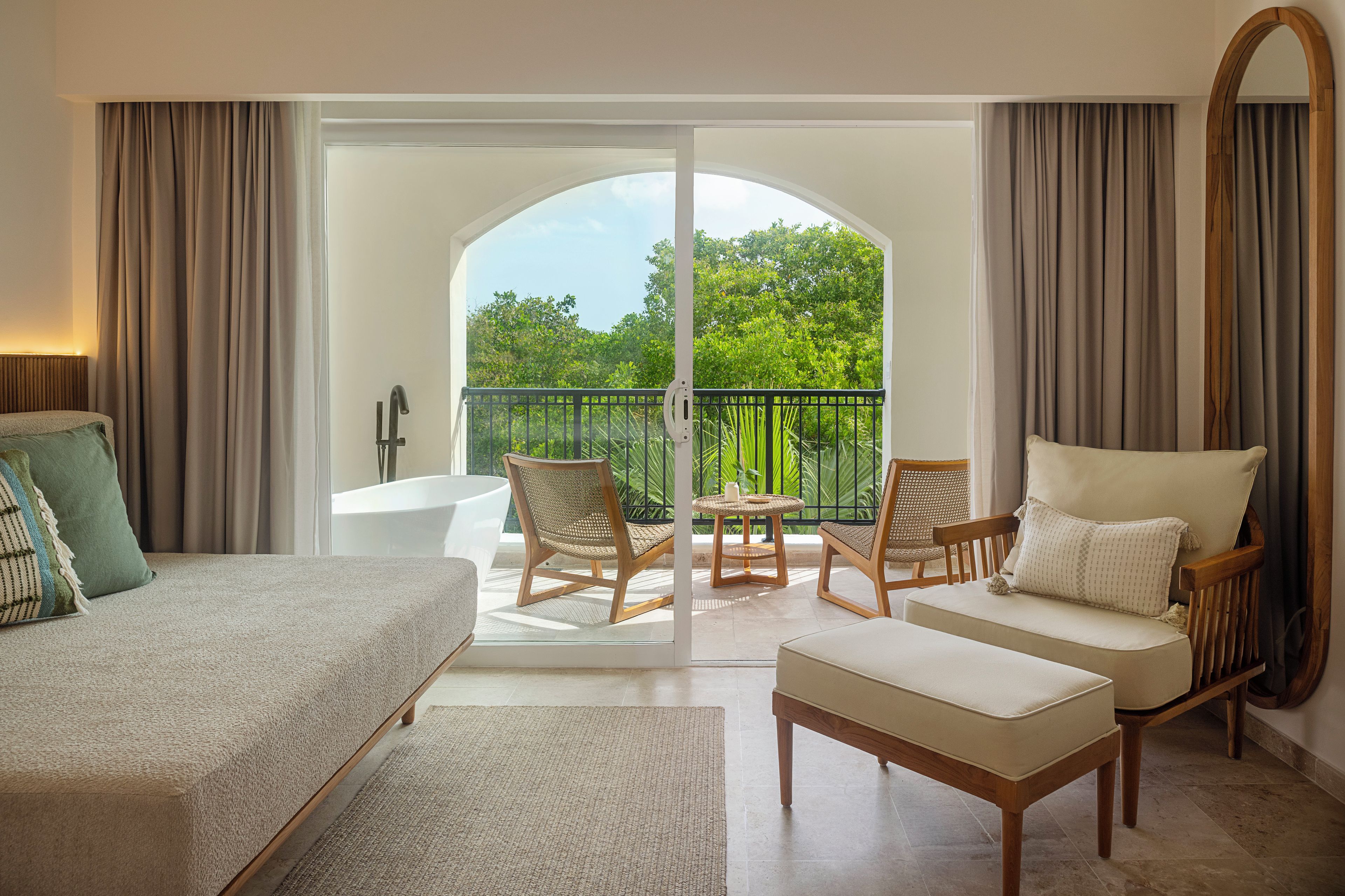 Habitación de hotel con cama, sofá, sillón, una mesita y balcón con vistas a zonas verdes.