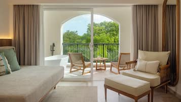Habitación de hotel con cama, sofá, sillón, una mesita y balcón con vistas a zonas verdes.