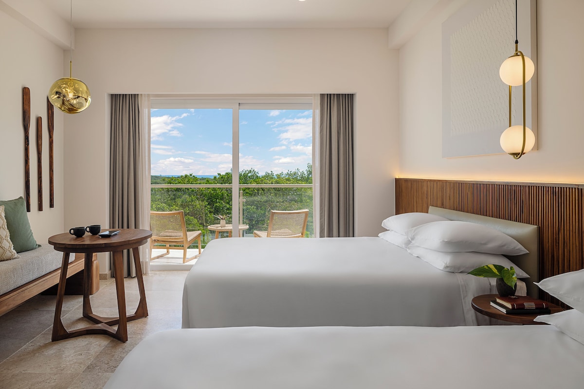 Habitación de hotel con dos camas, un sofá, una mesita y un balcón con vistas.