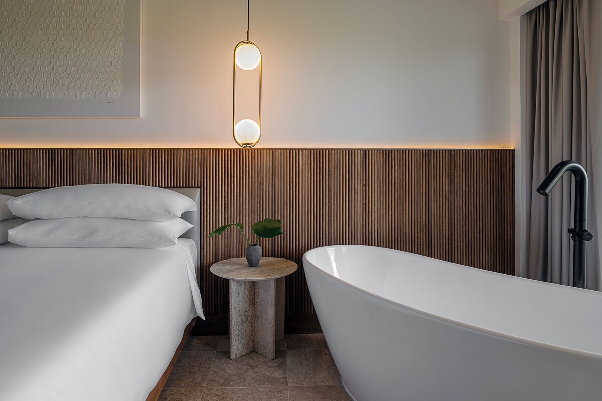 Ein modernes Badezimmer mit einer freistehenden Badewanne, einer Wand mit Holzlatten und einem Nachttisch mit Pflanze.