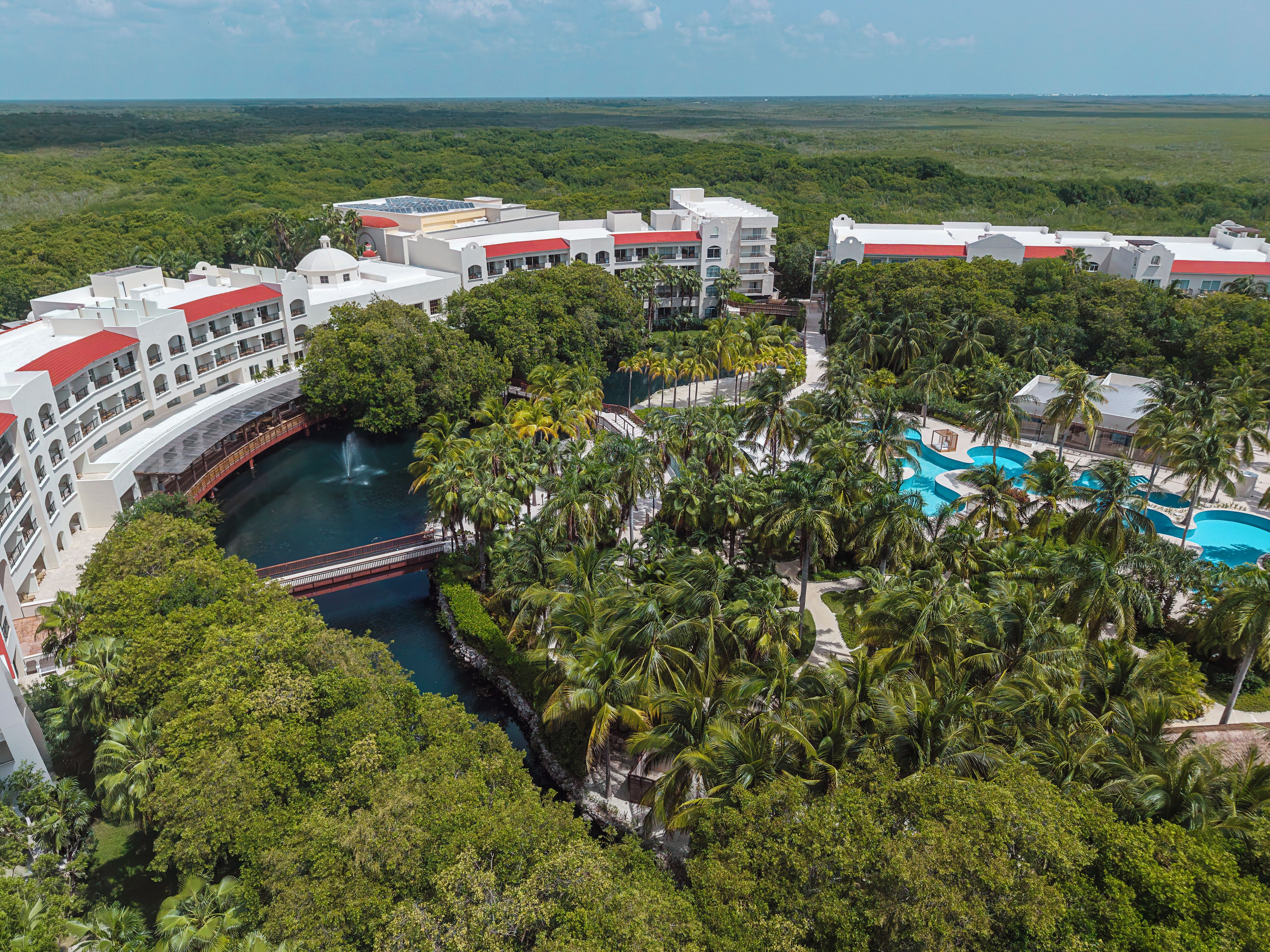 Un resort con varias edificaciones, una piscina y un puente sobre un elemento acuático.