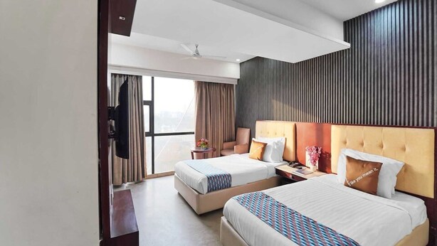 A hotel room with two beds, a large window, a flat-screen TV, and a wall-mounted panel. - Classic King Clubhouse Vytilla Kochi (Kanayannur)