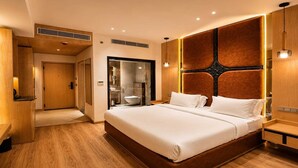 A modern hotel room with a large bed, wooden flooring, and a built-in wardrobe. - Classic King Clubhouse Vytilla Kochi (Kanayannur)