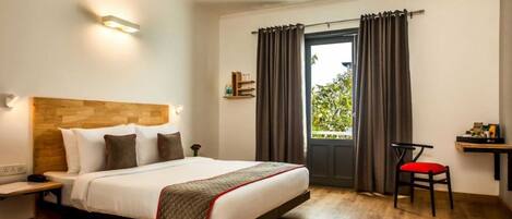 A hotel room with a bed, a desk, a chair, a ceiling fan, and a window with curtains.