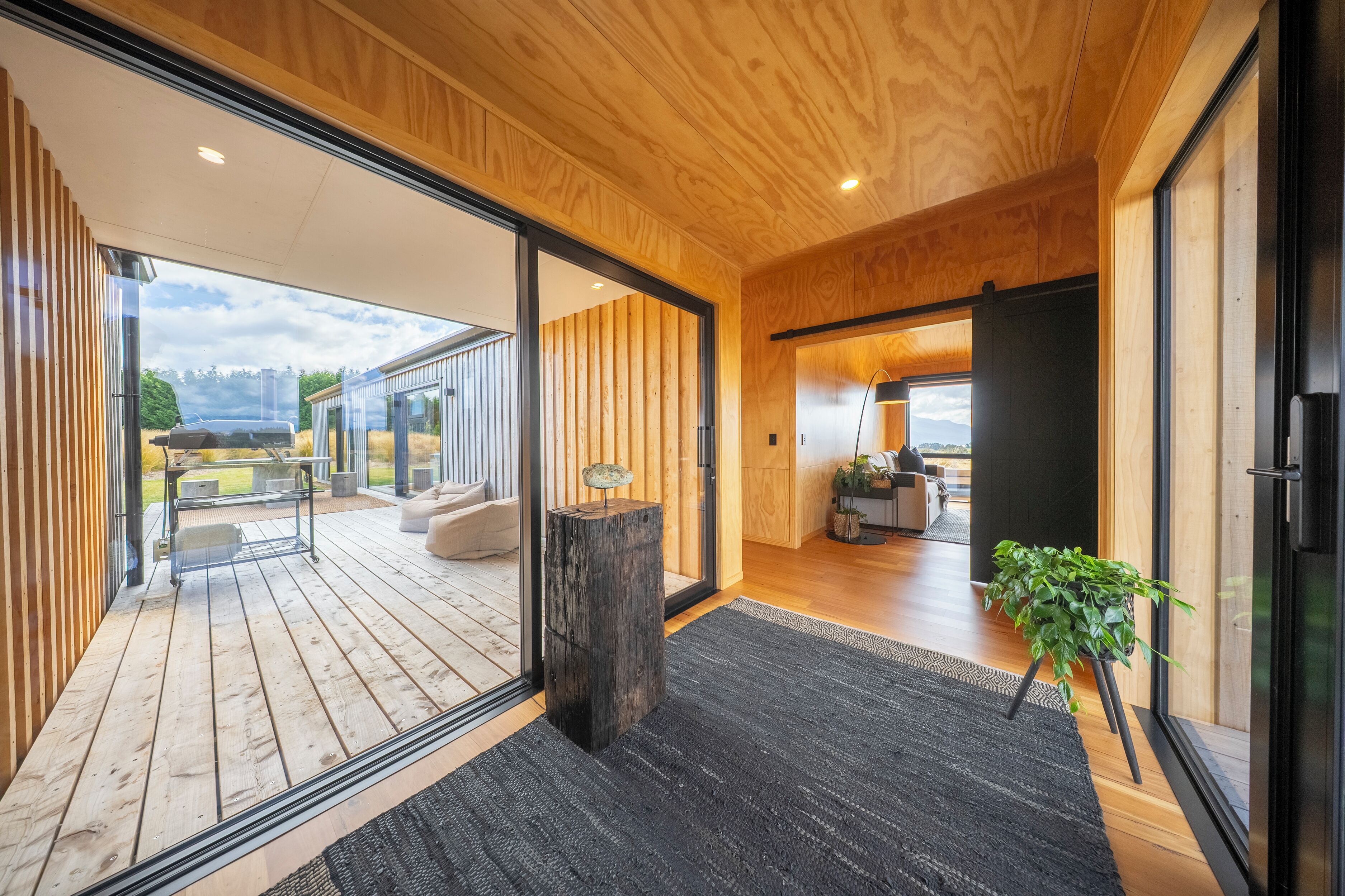 A modern interior with wooden flooring, a black rug, a wooden post, and a potted plant.