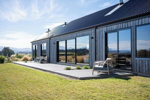 Un edificio moderno con grandes ventanales, un patio con mobiliario exterior y vistas al campo.