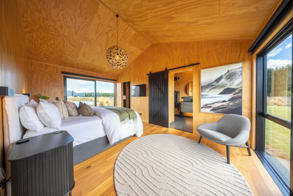 A modern bedroom with a bed, a chair, a round rug, and a large window with a view.