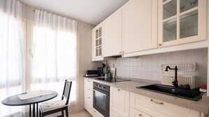 Een keuken met een eettafel, stoelen, een fornuis, oven en een spoelbak.