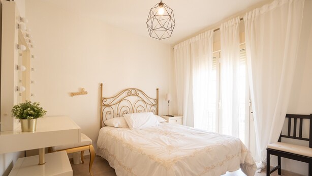 Een slaapkamer met een bed, nachtkastje, lamp, stoel en een spiegel met verlichting.