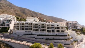 Ein modernes Mehrstöckhotel mit Balkonen, einer Steinsichtmauer und Blick auf eine gebirgige Landschaft.