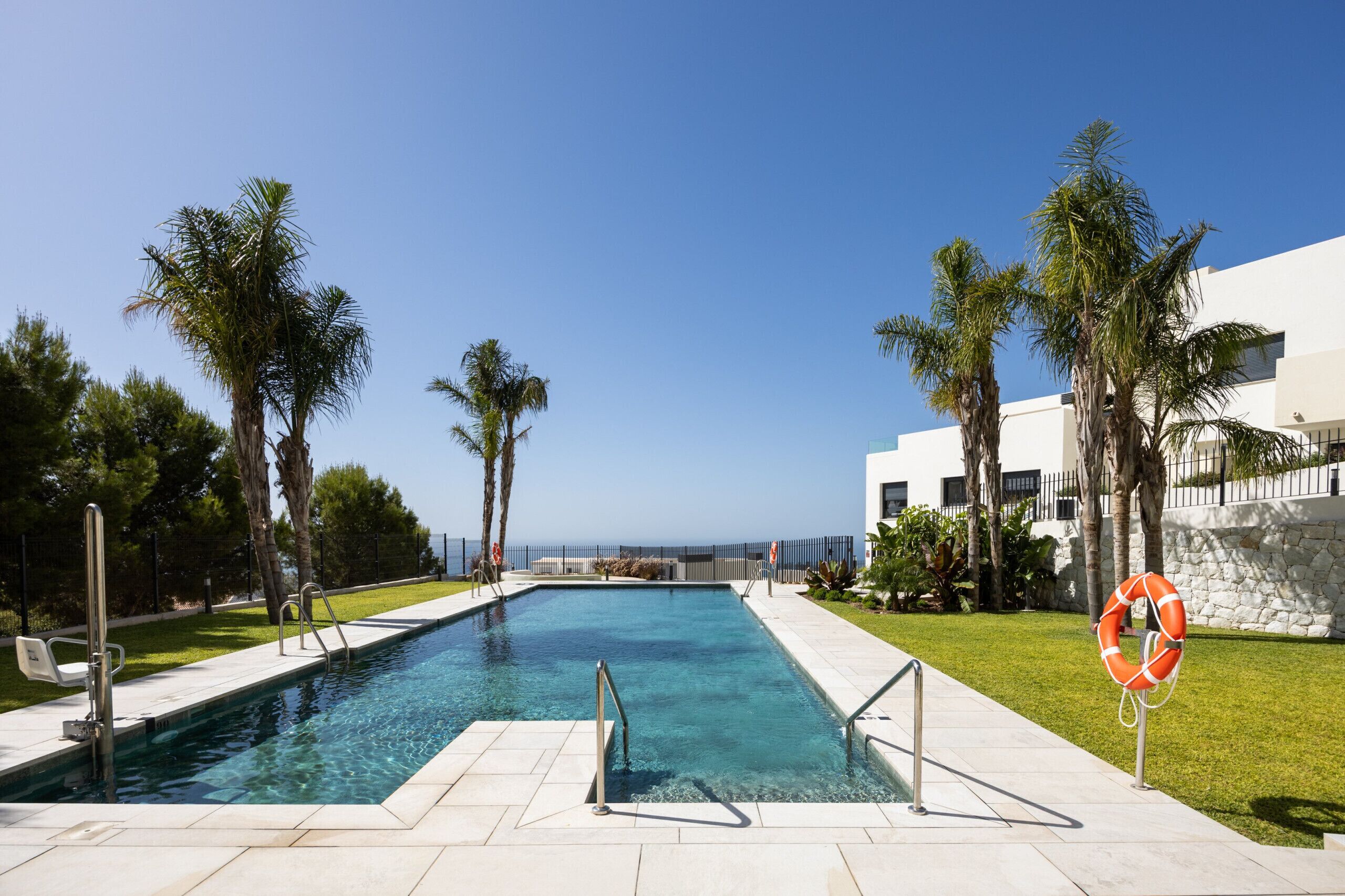 A swimming pool with a lifebuoy, surrounded by palm trees and a clear sky.