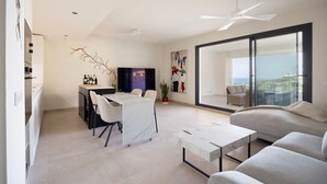 A modern living space with a dining area, a sofa, a coffee table, a TV, and a balcony with a view. - Horizonte Benalmádena - Brand-New 3-Bedroom Apartment (Benalmádena)