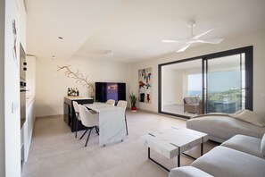 Ein modernes Wohnzimmer mit Essbereich, einer Couch, einem Couchtisch, einem Fernseher und einem Balkon mit Blick.