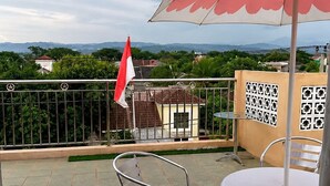 A terrace with metal chairs and tables, a flag, and a view of distant mountains. - Cozzy FK Heliconia (Jonggol)