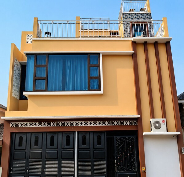 Un edificio de dos pisos con balcón, ventanas amplias y garaje con rejas decorativas.