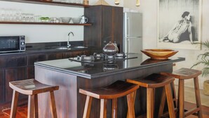 Una cocina moderna con una isla central, taburetes de bar, un refrigerador y una lámpara fijada a la pared.