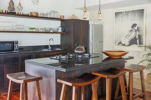 Eine moderne Küche mit einer zentralen Kochinsel, Barhocker, einem Kühlschrank und einer Wandleuchte.