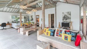 Amplia sala de estar con techo de madera, un sofá con cojines de colores, una mesa de comedor y un televisor.