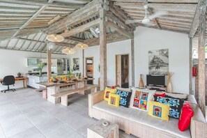 Ein großzügiger Wohnbereich mit Holzbalkendecke, einer Couch mit bunten Kissen, einem Esstisch und einem Fernseher.