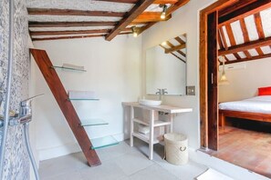 Ein Badezimmer mit einer Holztreppe, einem weißen Waschbecken, einem Spiegel und einem Bett mit einem roten Kissen.