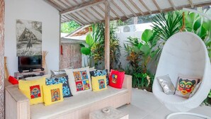 Un espacio de sala acogedor con un sofá, cojines, una silla colgante y un televisor.