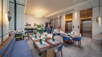 A modern dining area with tables set for service, a service staff member, and a visible elevator.