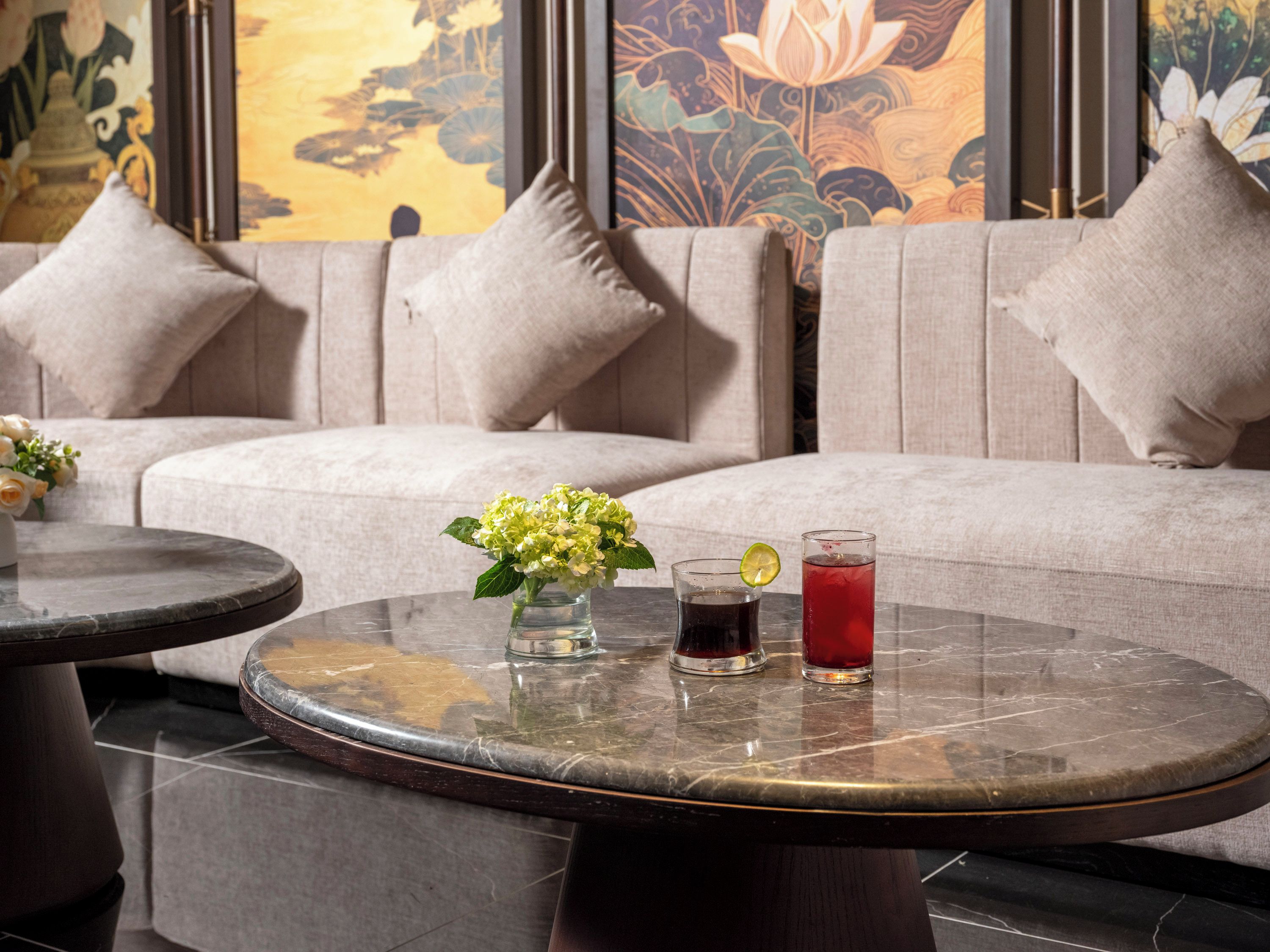 Un coin salon avec une table ronde, deux verres contenant des boissons et un vase de fleurs.