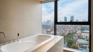 A modern bathroom with a large bathtub and a window offering a city view. - DUHORÉA hotel and wellness (Hanoi)