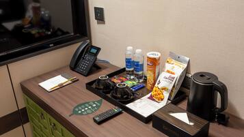 A hotel reception desk with a telephone, remote controls, a menu, bottled water, a salt packet, and a coffee maker.