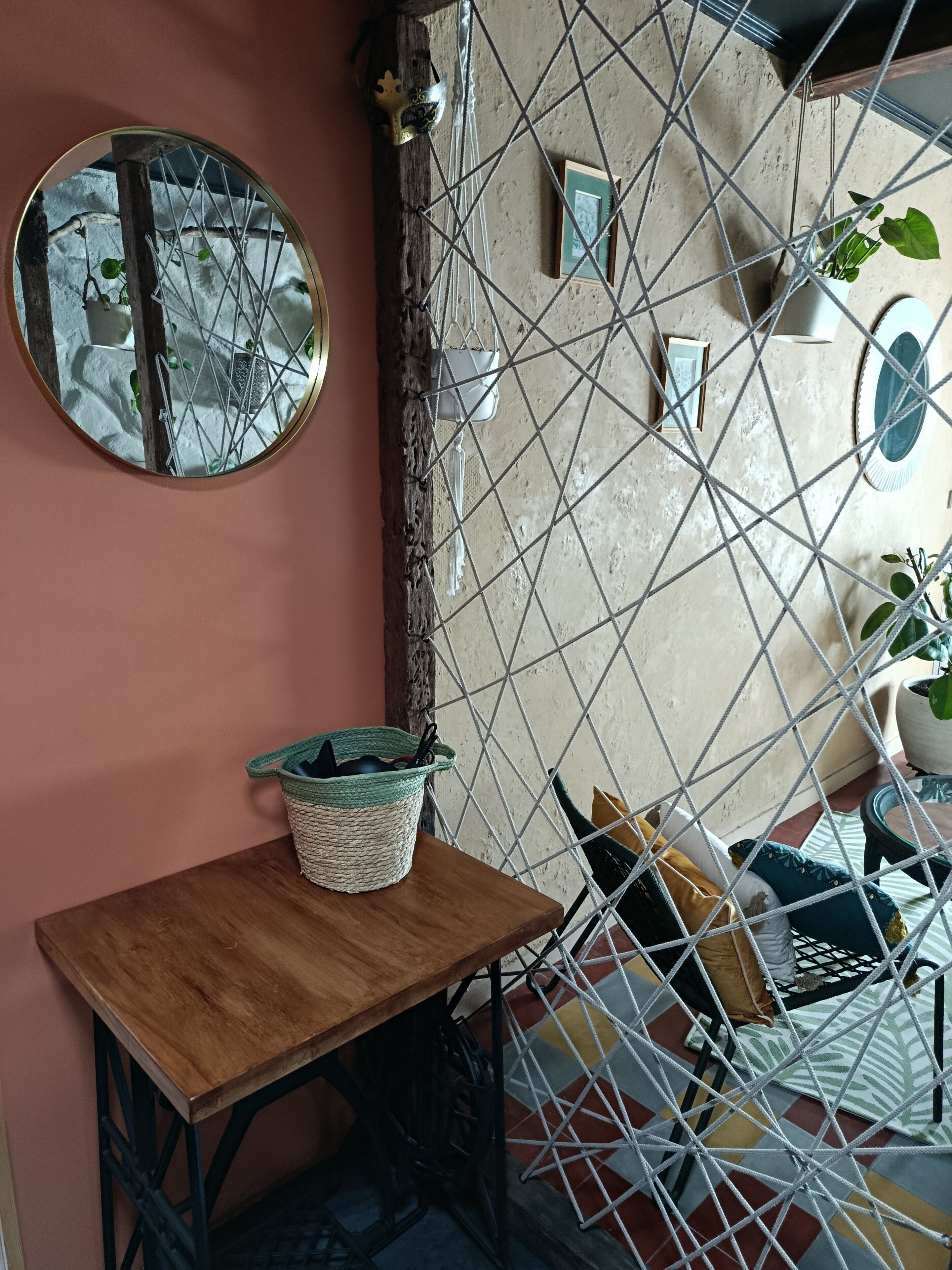 Una habitación con una mesa de madera, un espejo, una cesta de mimbre, una silla de metal y una hamaca.