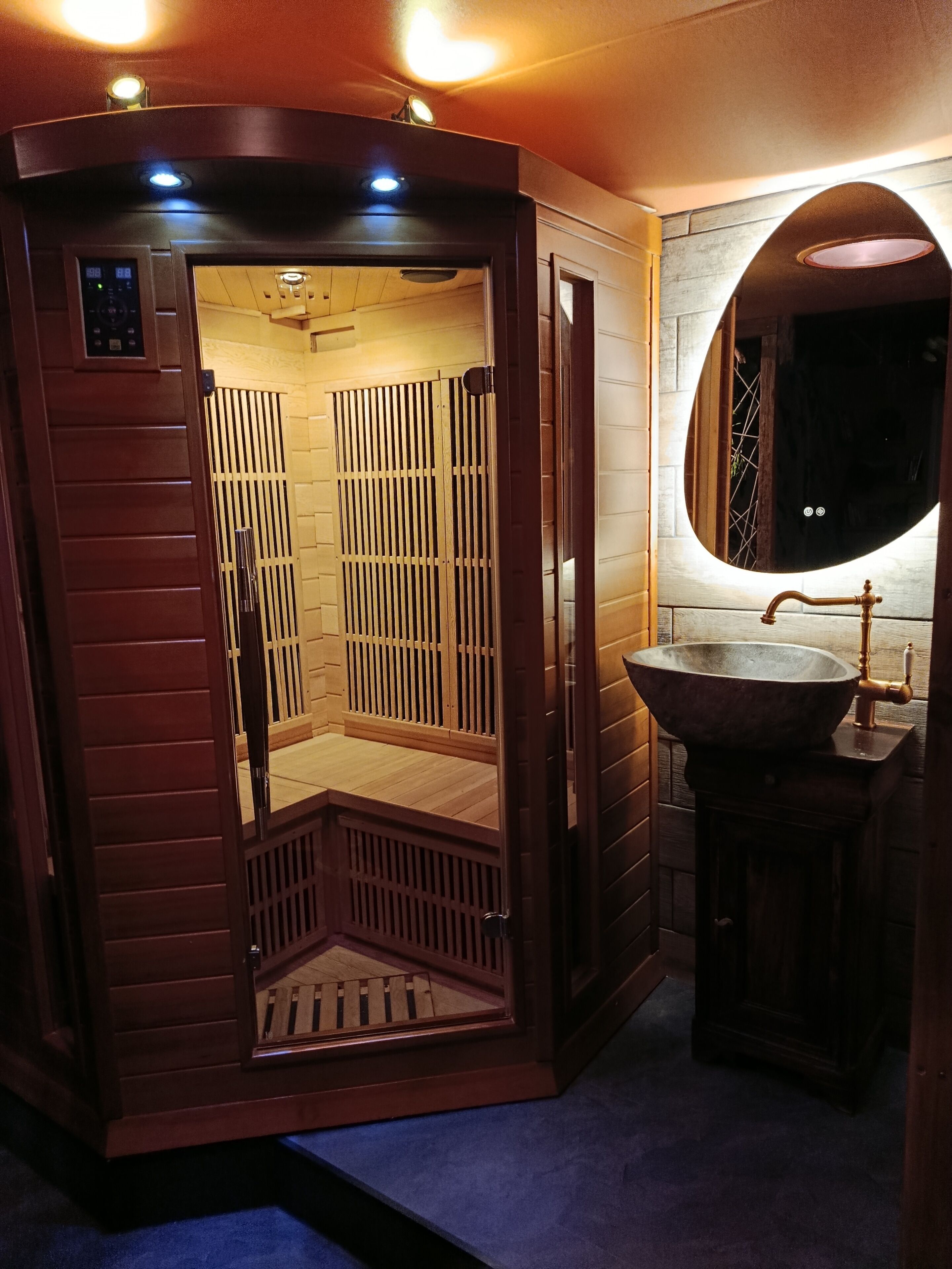 Una sauna con una porta in legno, un lavandino con bacino e uno specchio.