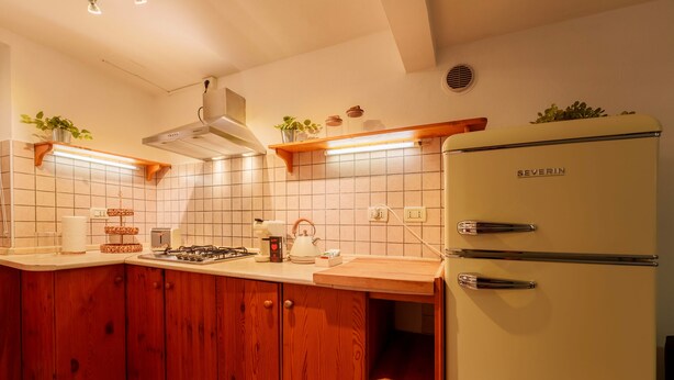 Una cocina con armarios de madera, salpicadero blanco de azulejos, refrigerador blanco y estufa a gas.
