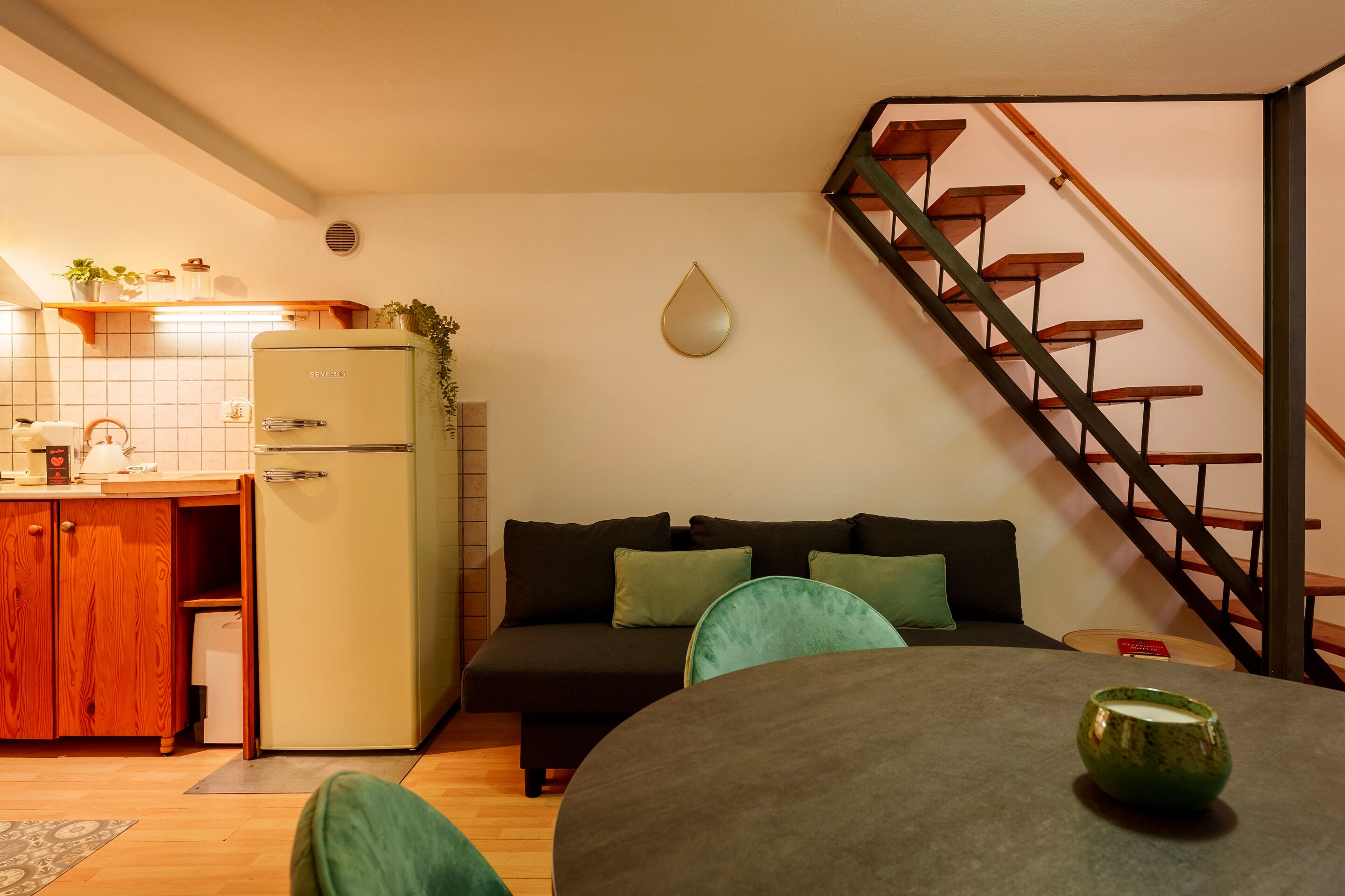 A compact living space with a kitchenette, a sofa, a dining table, and a staircase.