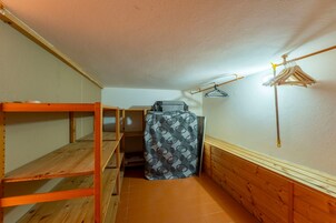 Un pasillo estrecho con literas de madera a un lado y un armario pequeño con una cubierta estampada al otro.