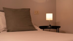 Una cama con un almohadón y una mesita de noche con una lámpara.