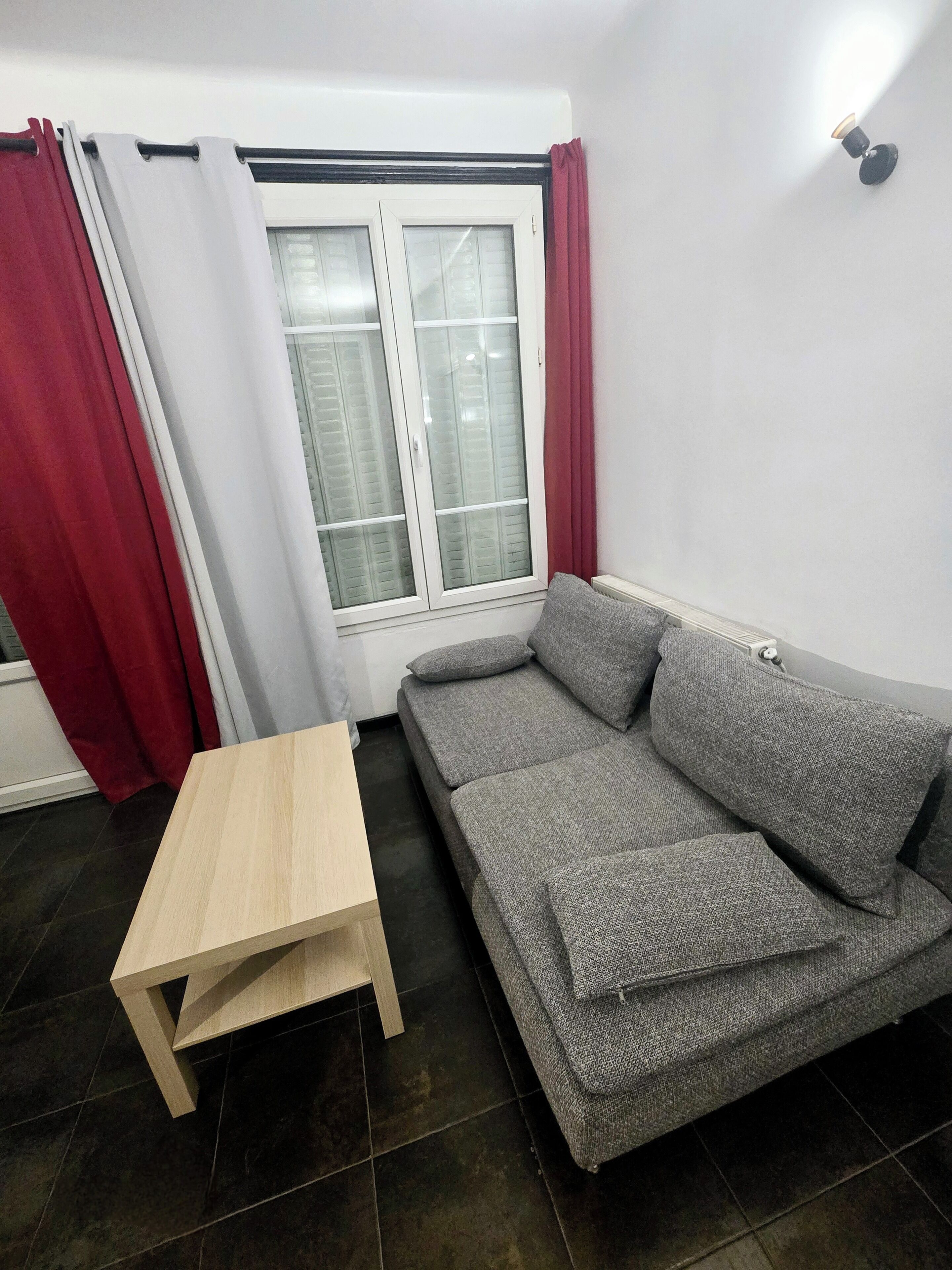 A room with a grey sofa, a small wooden table, and a window with curtains.