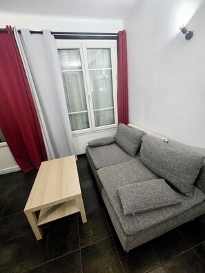 A room with a grey sofa, a small wooden table, and a window with curtains. - Beautiful 2-bedroom apartment in nice Gentilly neighborhood (Gentilly)