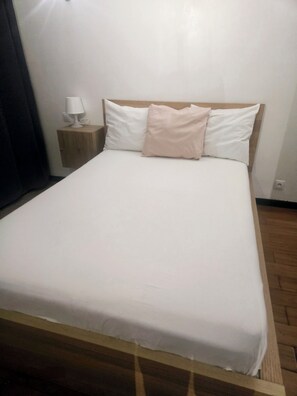 Ein Einzelbett mit Holzrahmen, ein Nachttisch mit Lampe und eine schlichte Wand.