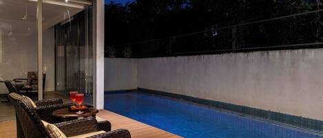 An outdoor swimming pool area with wicker furniture and a glass door leading to the interior.