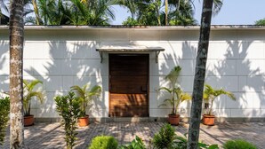 A building with a closed wooden door, surrounded by potted plants and a paved entrance area. - Staymaster Belamia•3BR•Private Pool (Parra)