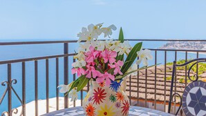 Ein runder Tisch mit Mosaikfliesenmuster, eine Vase mit Blumen und Blick aufs Meer.
