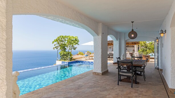 Ein Pool ohne Ende mit freiem Blick auf das Meer, ein Essbereich mit Außenbestuhlung und eine überdachte Terrasse mit Aussicht.