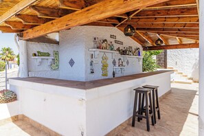 A bar area with a white wall, wooden ceiling, and a shelf with bottles. There are stools and a sign with motivational phrases. - Villa Mamma Mia, Luxury Villa with Panoramic Sea Views (Salobreña)