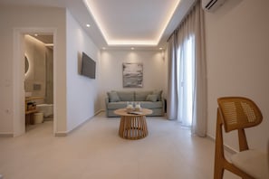 A modern living room with a sofa, a round wooden coffee table, and a television mounted on the wall. - GuVer Luxury Suites (Naxos)
