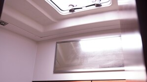 Une petite cuisine équipée avec une fenêtre au-dessus de l’évier, un miroir et un plan de travail.