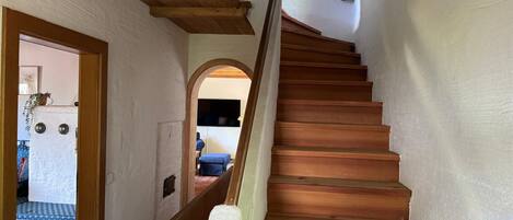 Una escalera de madera con barandilla que lleva a una habitación con cama y televisor.